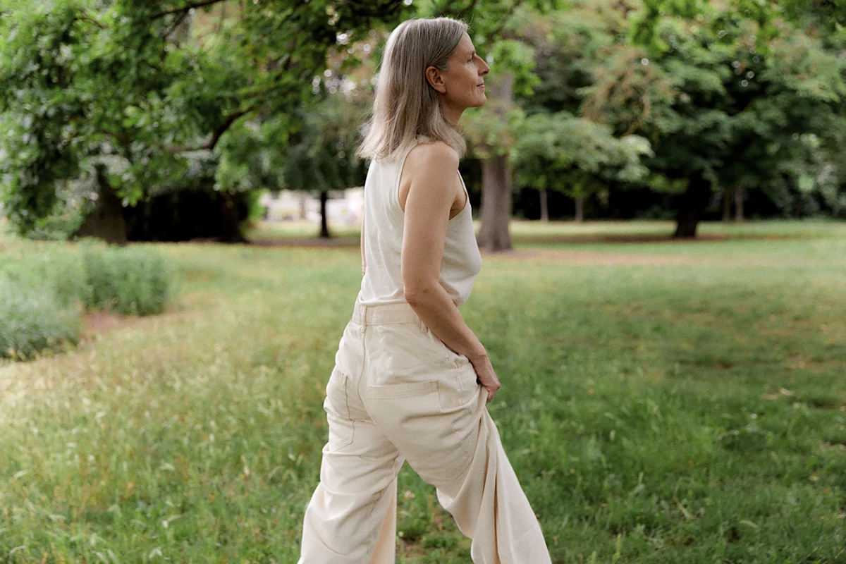 Middle-aged woman with natural silver hair wearing linen clothes, strolling through a green, lush park